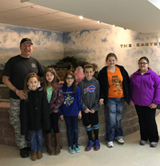 Group of students pose with a staff member in front of an exhibit